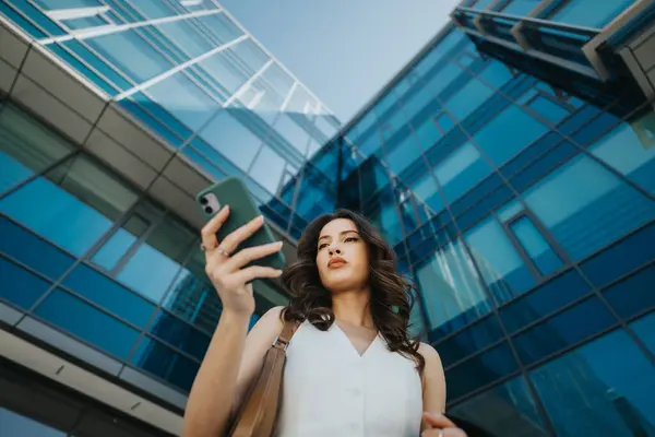 A professional businesswoman is engaged with her smart phone outside modern office buildings, reflecting ambition and connectivity.