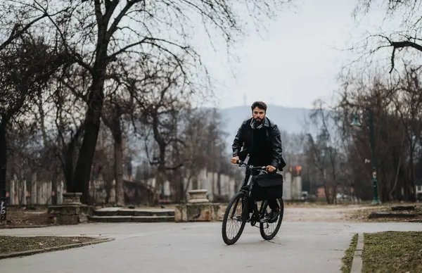 Stylish businessman rides a bicycle while working outdoors in an urban park, blending business with a natural vibe.