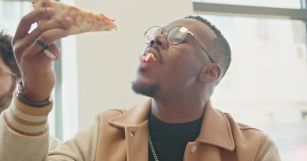 スタイリッシュな若い男は 彼がおいしいピザのスライスに噛まれるので 楽しみの瞬間にキャプチャされます — ストック動画