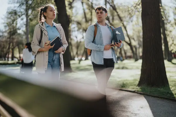 A male and a female student or friends carrying textbooks in a park, engaging in a discussion with a backdrop of green trees.
