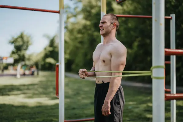 stock image A young shirtless man working out with a resistance band in a park, focusing on strength training and fitness.