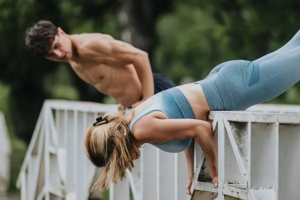 stock image Healthy young individuals performing fitness exercises on a bridge in an outdoor park setting, focusing on arms and legs workout.