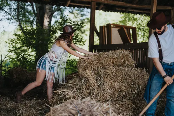 stock image A young couple working together in a barn, stacking hay bales. They are enjoying a rustic farm lifestyle.