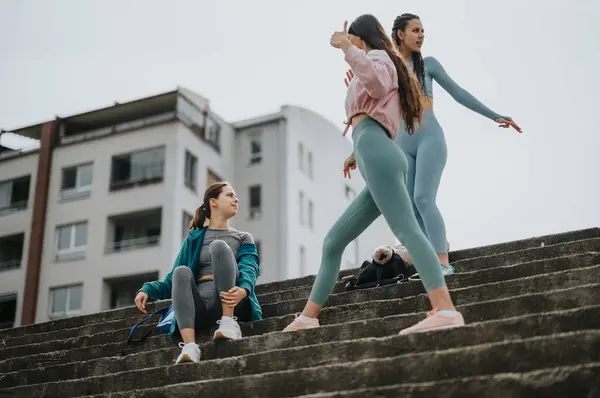 stock image Two athletic friends in fitness attire resting during a workout on concrete steps with a cityscape backdrop.