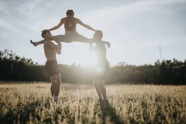 stock image Young, fit girl doing a front split on her friends shoulders outdoors in a sunlit field. Artistic display of strength and flexibility.