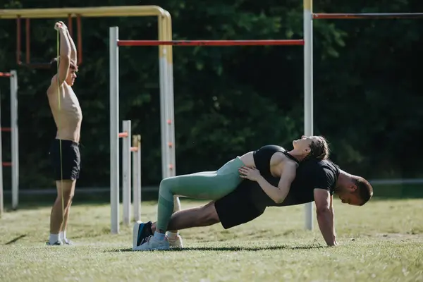 stock image Athletes engage in outdoor fitness routines, performing partner strength exercises and individual stretching. Capture the essence of teamwork and dedication in a natural outdoor setting.