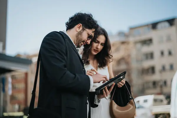 stock image Two professional colleagues engaged in a serious discussion, analyzing statistics on a tablet during an outdoor meeting in the city.