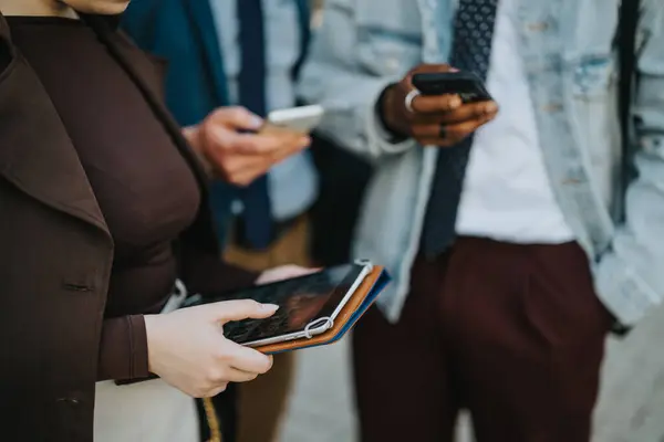 stock image A group of business professionals focused on their smart phones and tablets during an outdoor break, illustrating modern connectivity and work-life integration.