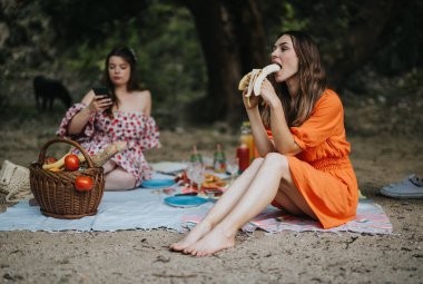 Two young women enjoying a relaxing picnic outdoors, featuring fresh fruits and laid-back atmosphere. Perfect representation of leisure and friendship. clipart