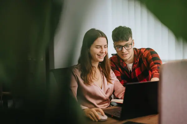 stock image A young man and woman, viewed as business colleagues, engage in a focused discussion over a laptop, suggesting a collaborative work environment. The setting is casual yet professional, depicting