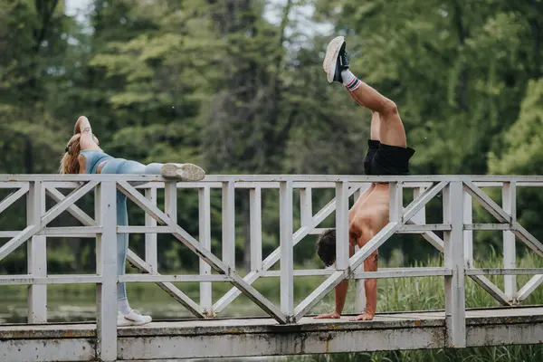 stock image Fit couple performing handstands on a bridge during an outdoor workout. Fitness enthusiasts exercising in nature, showcasing strength, balance, and an active lifestyle.