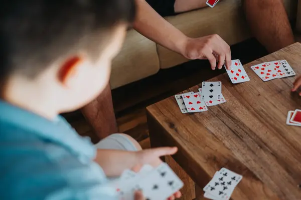 stock image Boys play a card game on a wooden table, enjoying their leisure time indoors. Fun and competitive game activity among friends.