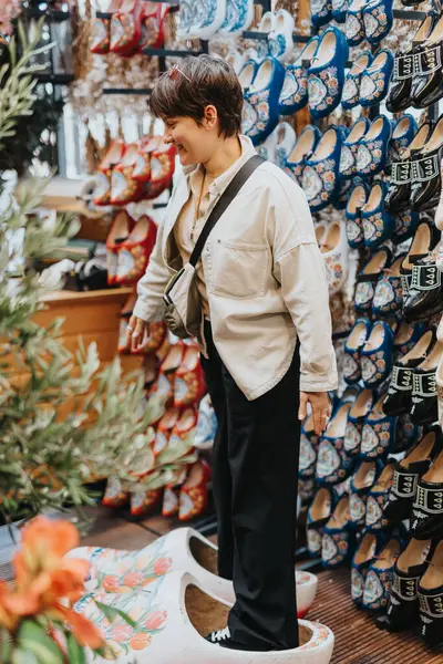 stock image Person exploring a traditional Dutch souvenir shop, standing in oversized decorative wooden clogs amidst a colorful display of patterned shoes.