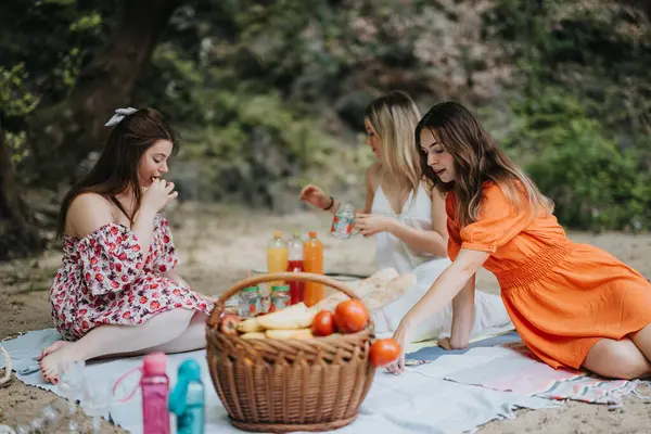 stock image Three girls enjoy a summer picnic in a park, surrounded by food and drinks, conveying friendship and relaxation.