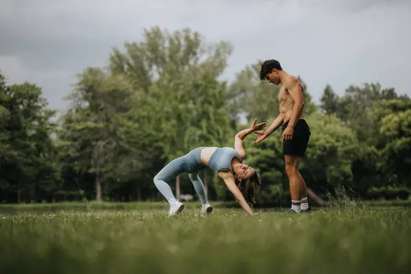 stock image Athletic couple performing acrobatic exercises in a park. Man and woman practicing fitness activities together in nature.