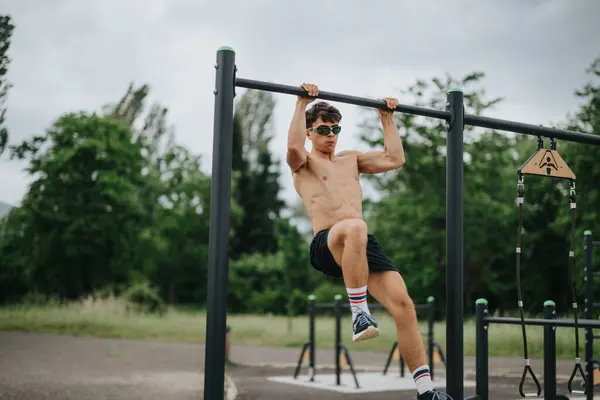 stock image Young man performing pull-ups on parallel bars in an outdoor park. Fitness, strength training, and calisthenics exercise concept.