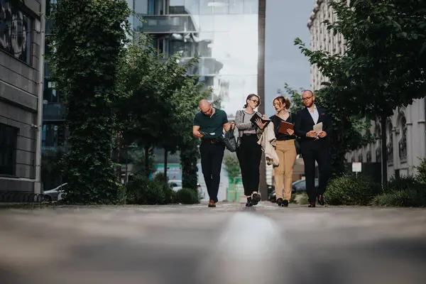 stock image Group of business people walking and discussing work in a modern urban setting surrounded by office buildings.