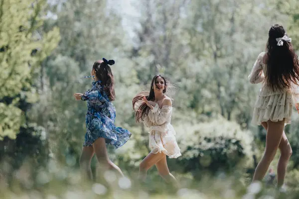 stock image Three young women, expressing freedom and joy, run playfully in a lush green park. Their light, flowing dresses and carefree laughter embody a perfect springtime day.