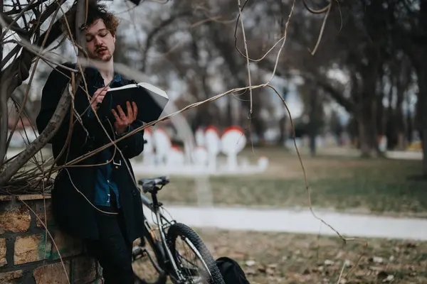 stock image A business-oriented young professional remotely working outdoors with a bicycle, using a notebook.