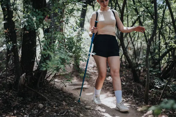 stock image Young woman hiking on a sunny day through a forest trail, enjoying nature and adventure. Exploring outdoors, she is happy and having fun.