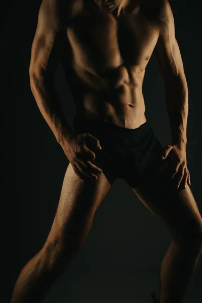 stock image Fit man showing his abs and muscular physique in a dark studio setting, highlighting strength and fitness.