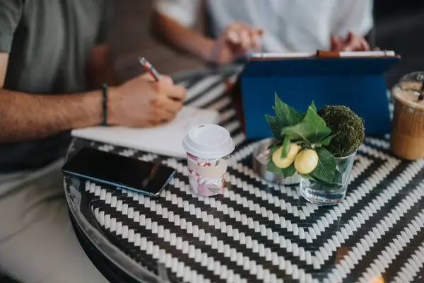 stock image Business meeting in a coffee shop with participants utilizing notebooks, tablets, and coffee cups on a stylish table. Engaged discussions and note-taking.