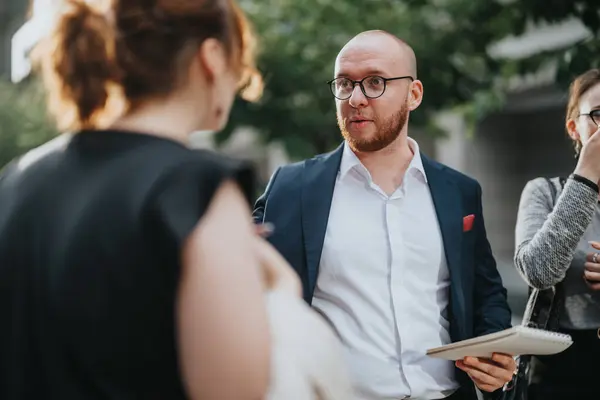 stock image Three professionals have a business discussion outdoors. The main subject is a bald man in a suit holding a notebook, engaging with two other individuals.