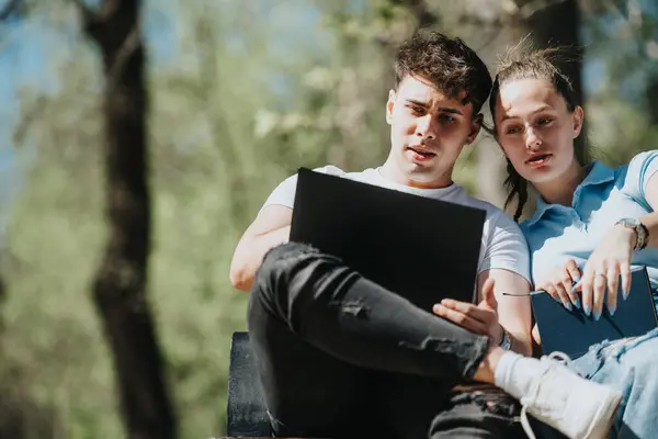 Stock image Two young friends focused on their studies and discussing ideas while seated outdoors, surrounded by greenery.