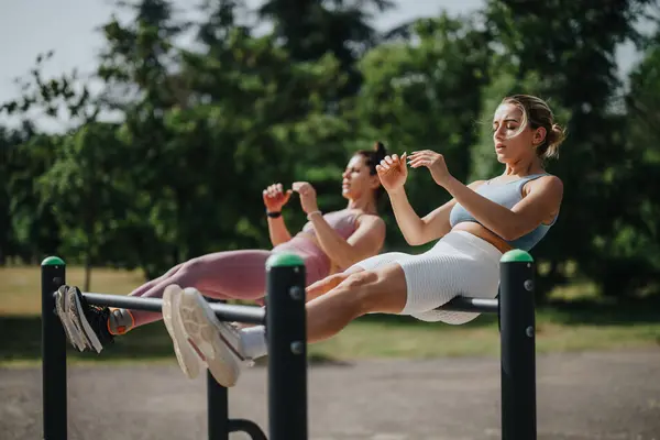 stock image Two women are engaged in a calisthenics workout in a park, focusing on core exercises and fitness. The outdoor setting promotes health and well-being.