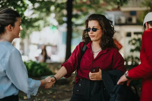 Stock image Young business associates meeting and shaking hands outdoors in a park setting, highlighting professional interaction and connection.