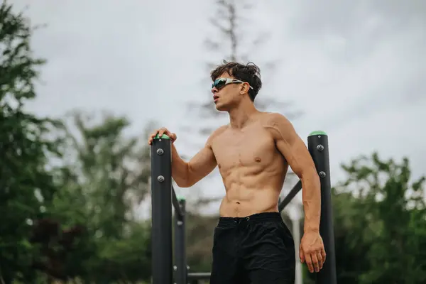 stock image Fit young man performing workout on parallel bars at outdoor gym. Focused on health and fitness in a natural environment.