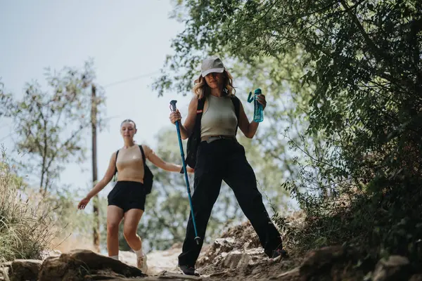 stock image Two young women happily hiking in a lush forest on a sunny summer day, embracing nature and adventure.