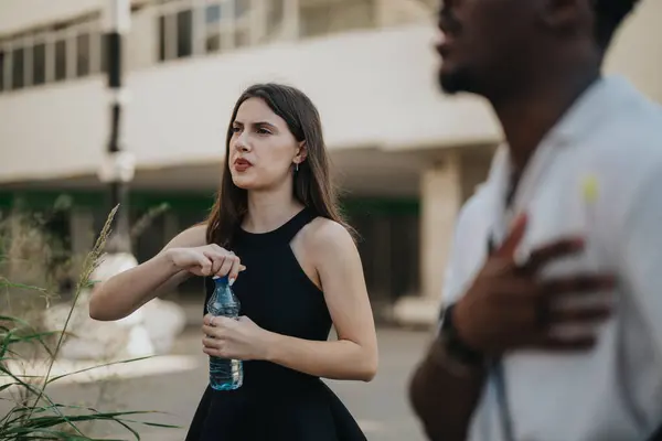 stock image Mixed race people discussing business outdoors in the city. Focused businesswoman holding a water bottle.