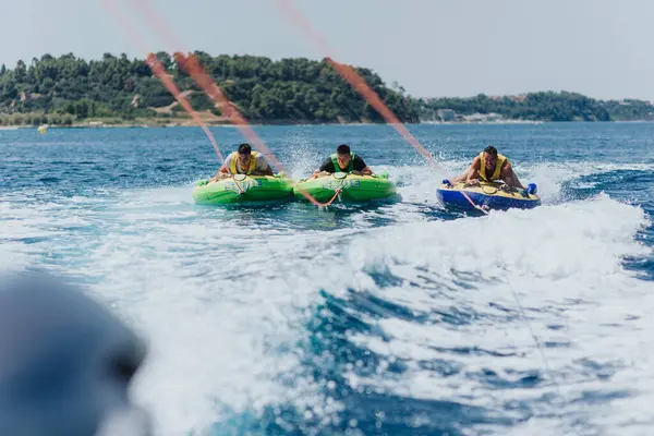 stock image Three friends enjoy an exhilarating speedboat tubing adventure on a sunny day in clear blue waters.