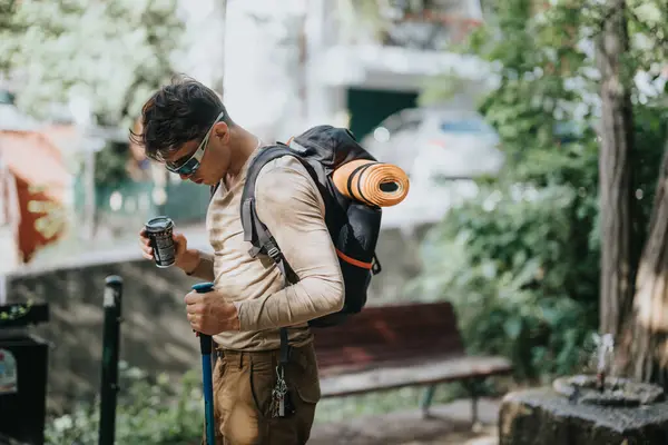 stock image Young man taking a coffee break during a hike in an urban park, equipped with hiking gear and a backpack.