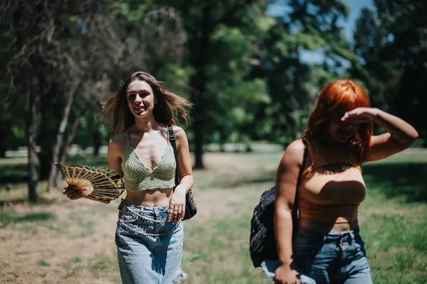 stock image Two young women walking through a park on a sunny day, smiling and enjoying the pleasant weather, surrounded by lush greenery.