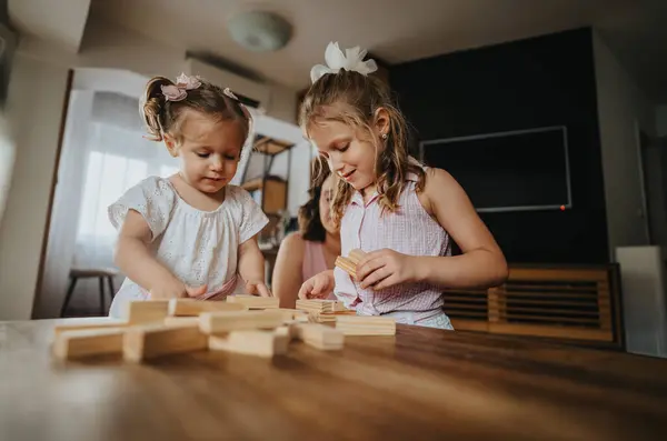 stock image Two young sisters happily playing with wooden blocks at home, building together and enjoying creative family time in a cozy indoor setting.