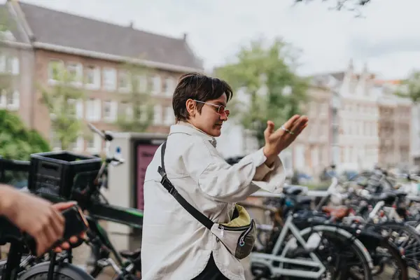 stock image A person wearing sunglasses and a white jacket gestures while walking near bicycles in a city. The scene captures a city vibe and casual interaction.