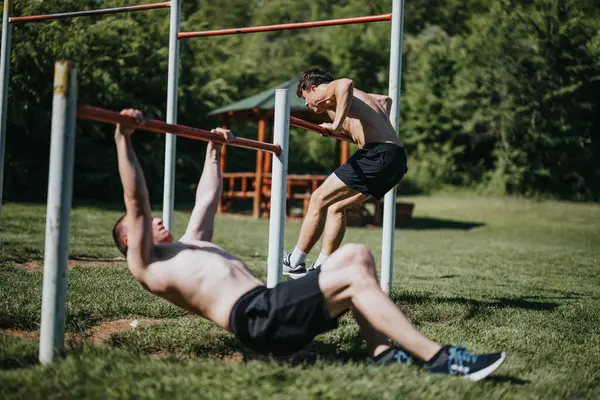 stock image Two young men are working out in an urban park, utilizing outdoor fitness equipment for strength training exercises.