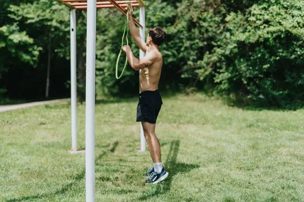 stock image Fit man exercising in nature using a resistance band for strength training. The scene depicts outdoor fitness and a healthy lifestyle.