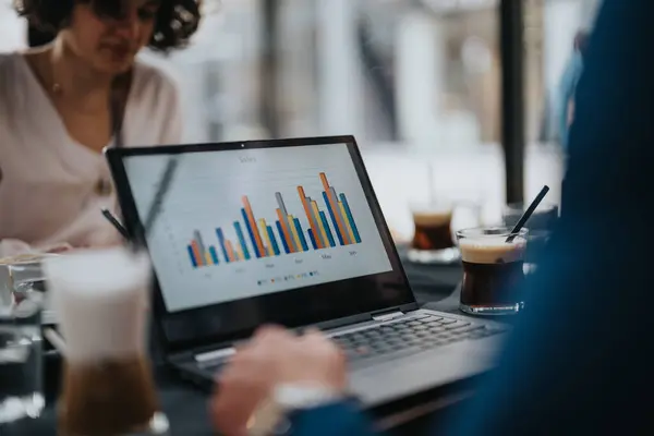 stock image Colleagues in an coffee bar meeting reviewing a sales chart on a laptop screen with coffee cups on the desk.