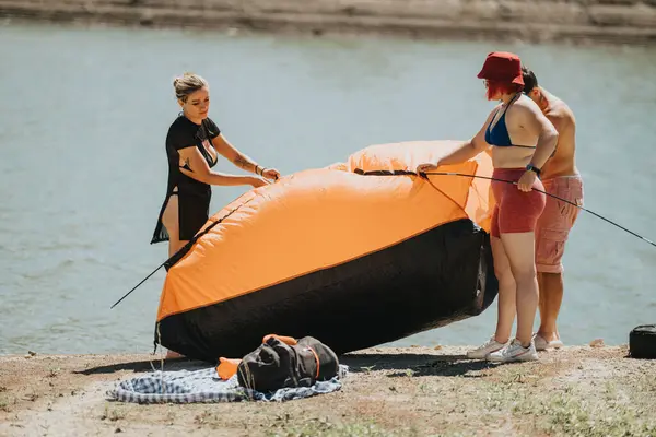 stock image Friends having fun setting up an inflatable tent by the lake on a sunny summer day. Outdoor activities and relaxation in nature.