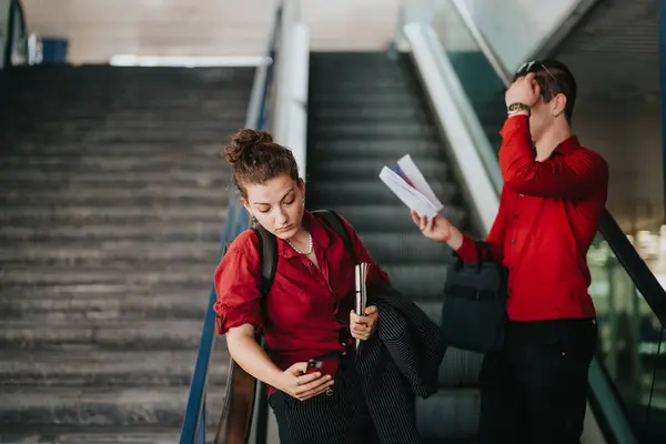 stock image Business professionals in red shirts using smart phones on an escalator in a city setting. Modern business communication and commuting.