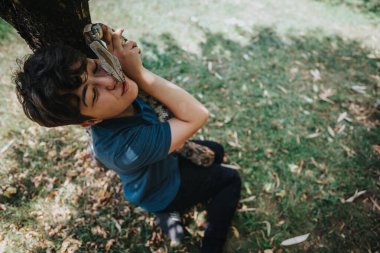 A girl is sitting outside under a tree, playing with a snake and showing a connection with nature and animals. clipart