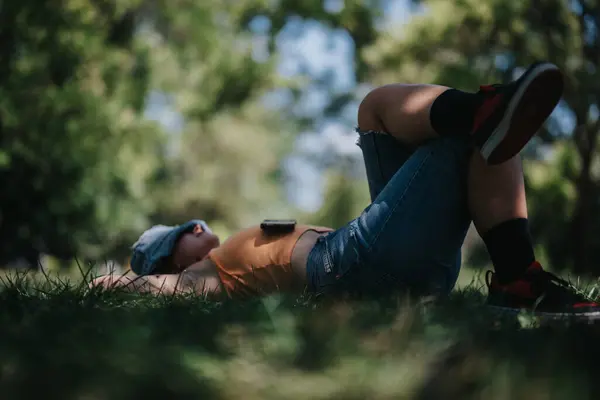 stock image Relaxed person laying on grass in a summer park, appreciating nature and tranquility. A peaceful outdoor moment under the trees.