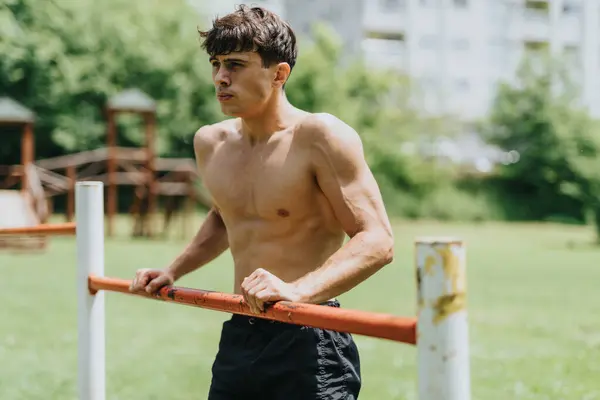 stock image Fit man exercising in nature at an outdoor gym performing dip exercises on a sunny day in a park.