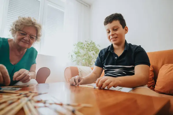 stock image A young boy enjoys a game of pick-up sticks with his grandmother in a cozy living room, highlighting family bonding and leisure time at home.