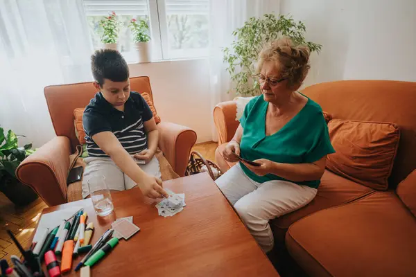 stock image A grandmother and her grandson are playing a card game in a cozy living room setting, fostering family bonding and spending quality time together.