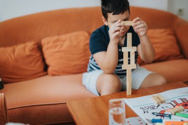 A young boy enjoys playing with building blocks at home while his grandmother knits nearby, creating a cozy family atmosphere. clipart