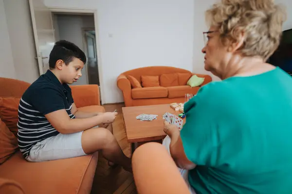 stock image A young boy and his grandmother engaging in a card game in a warm, cozy living room atmosphere, highlighting family bonding and quality time.